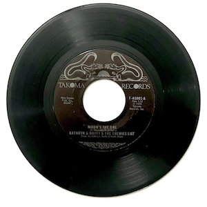 May include: A black vinyl record with the label "TAKOMA RECORDS." The label features the text "NIXON'S THE ONE" by Kathryn & Duffy & The Enemies List. The record is a 45 RPM single.