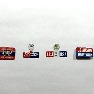 May include: Four vintage political campaign pins. The pins feature the names "Johnson-Humphrey" and "LBJ" with the words "USA" and "Vote Democratic". The pins are red, white, and blue.