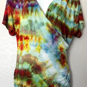 May include: A colorful tie-dye wrap top in shades of red, yellow, green, blue, and purple. The short-sleeved shirt has a V-neck and a gathered side. The fabric is a soft, flowing material.