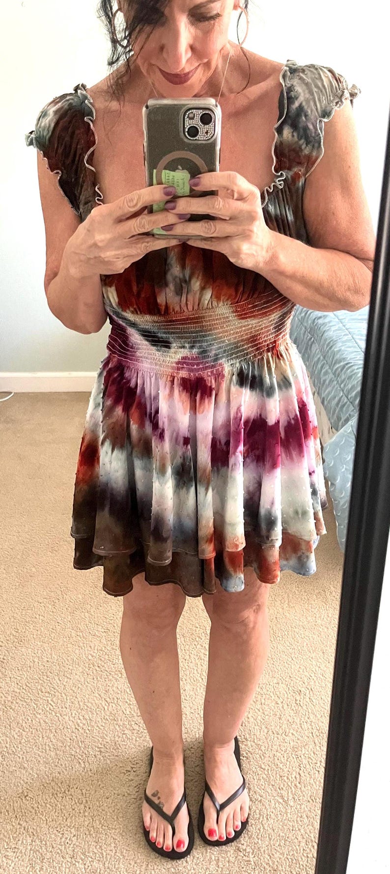 K&ouml;nnte beinhalten: Ein Mini-Kleid mit Batikmuster und R&uuml;schenausschnitt und -rock. Das Kleid hat eine Mischung aus Farben, darunter Rot, Wei&szlig;, Braun und Blau. Die Person tr&auml;gt schwarze Flip-Flops.