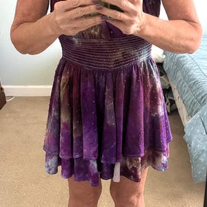 Puede incluir: Un vestido morado con corpi&ntilde;o de terciopelo y falda en capas. El vestido tiene cintura entallada y falda fluida. La persona lleva chanclas negras con esmalte de u&ntilde;as rojo.
