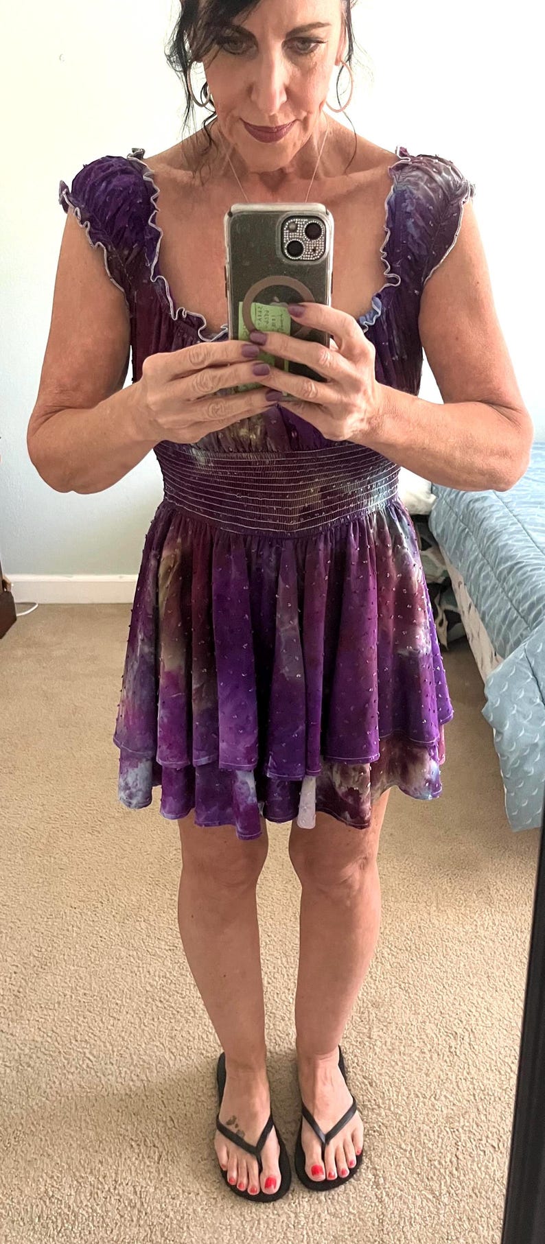 Puede incluir: Un vestido morado con corpi&ntilde;o de terciopelo y falda en capas. El vestido tiene cintura entallada y falda fluida. La persona lleva chanclas negras con esmalte de u&ntilde;as rojo.