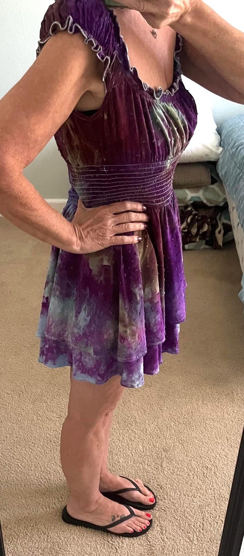 Puede incluir: Un minivestido de terciopelo en tonos morados, azules y marrones. El vestido presenta un corpi&ntilde;o ajustado con cintura ce&ntilde;ida y una falda escalonada. El escote y las mangas tienen un ribete con volantes.