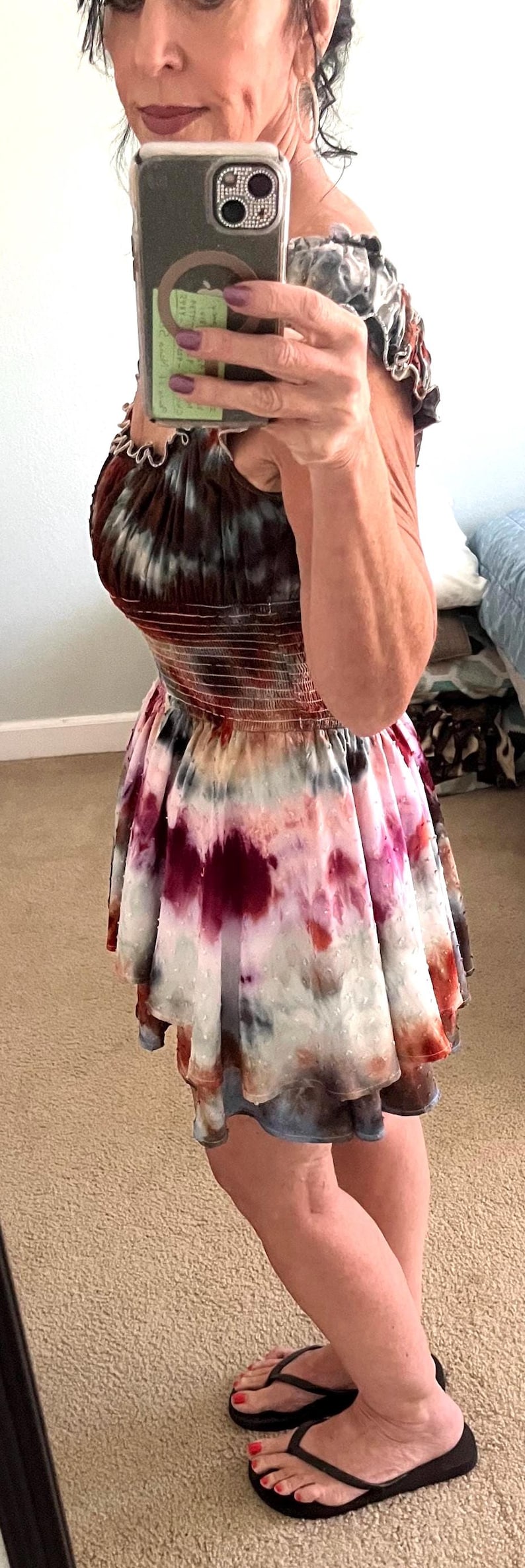 K&ouml;nnte beinhalten: Ein Batik-Kleid mit ger&uuml;schtem Ausschnitt und ausgestelltem Rock. Das Kleid hat eine Mischung aus Farben, darunter Burgunderrot, Rosa und Wei&szlig;. Die Person tr&auml;gt schwarze Flip-Flops.