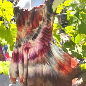 K&ouml;nnte beinhalten: Ein Batik-Kleid in Rot-, Braun-, Lila- und Gr&uuml;nt&ouml;nen. Das Kleid hat einen ger&uuml;schten Ausschnitt und ein figurbetontes Oberteil mit elastischer Taille. Der Rock ist ausgestellt und hat ein gepunktetes Muster.