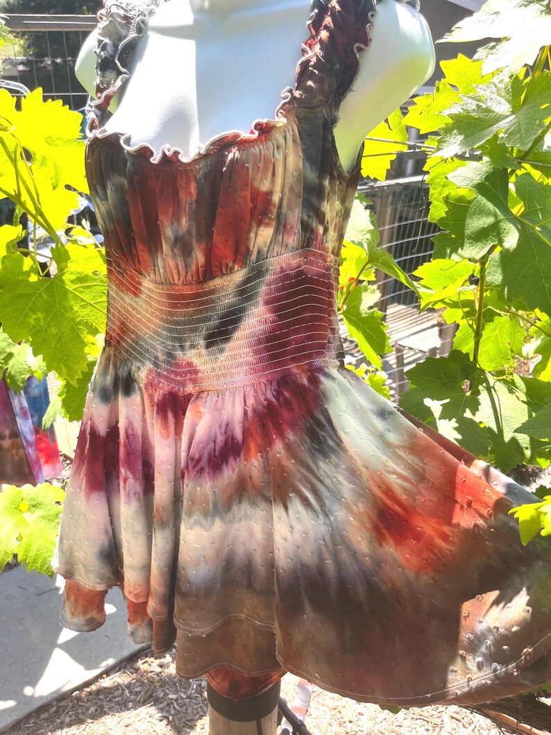 K&ouml;nnte beinhalten: Ein Batik-Kleid in Rot-, Braun-, Lila- und Gr&uuml;nt&ouml;nen. Das Kleid hat einen ger&uuml;schten Ausschnitt und ein figurbetontes Oberteil mit elastischer Taille. Der Rock ist ausgestellt und hat ein gepunktetes Muster.