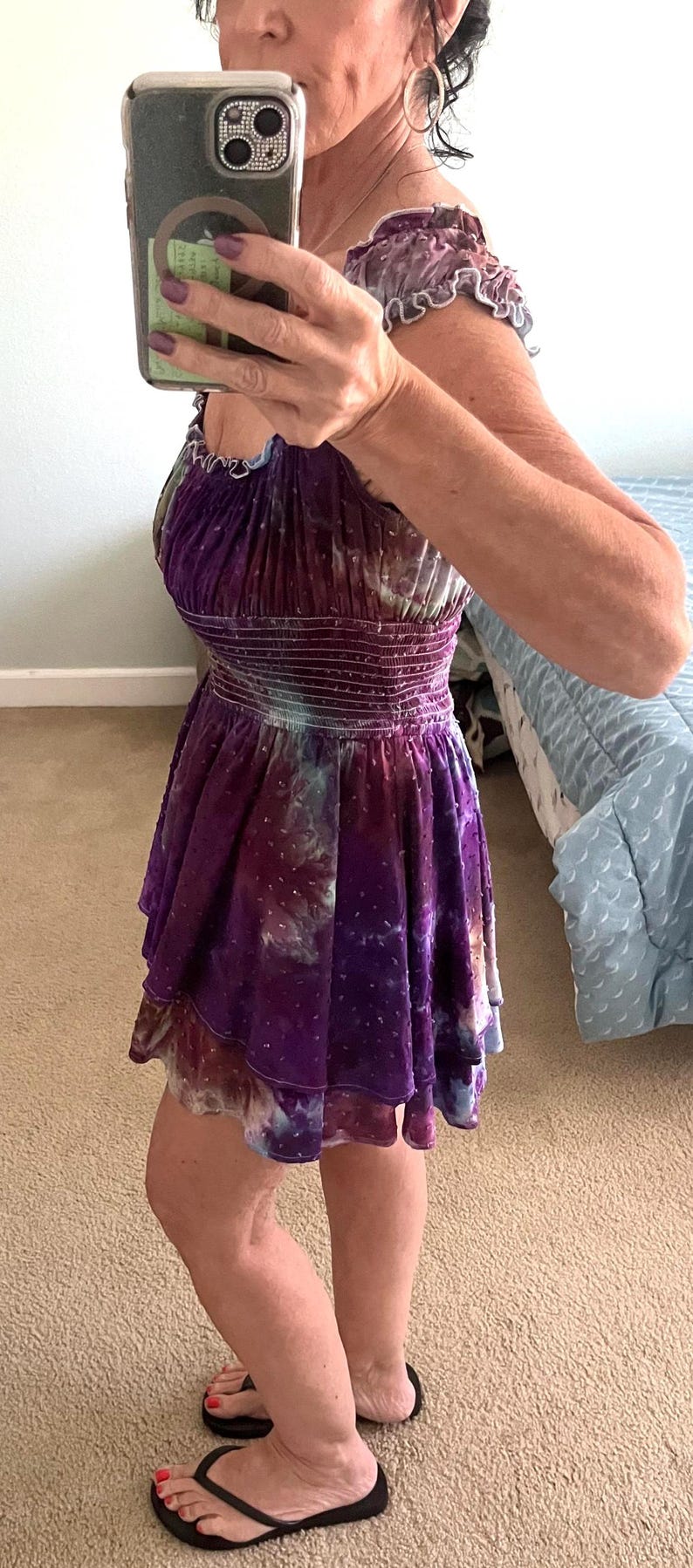 Puede incluir: Un vestido morado y azul te&ntilde;ido con un estampado tie-dye con una falda escalonada. El vestido tiene un corpi&ntilde;o ajustado con cintura fruncida y mangas cortas con volantes. La persona lleva chanclas negras.