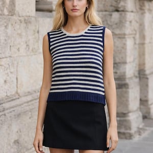 May include: A sleeveless, navy blue and white striped sweater with a crew neck. The sweater is paired with a black mini skirt. The outfit is suitable for casual wear.