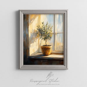 Pode incluir: Uma impressão de arte emoldurada retrata uma oliveira em vaso em uma janela ensolarada. A obra de arte apresenta uma paleta de cores quentes e uma moldura prateada. O texto "Rossignol Studio" e "Art Prints That Bring Walls To Life" está na parte inferior.