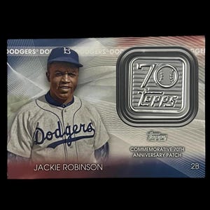 May include: A commemorative baseball card featuring Jackie Robinson in a Dodgers uniform. The card includes the text "Dodgers" and "Jackie Robinson." A silver emblem reads "70 Topps" with "Commemorative 70th Anniversary Patch" text.
