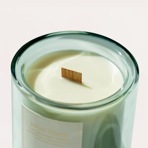 May include: A clear glass candle holder with a pale green tint, filled with creamy white wax. A wooden wick is in the centre. The label reads "Inner Peace".