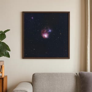 May include: A framed print of a nebula in space. The image features a dark background with numerous stars and a central nebula with shades of pink, red, and blue. The frame is a dark brown color.