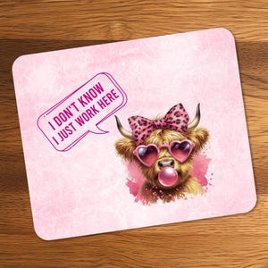 Könnte beinhalten: Ein quadratisches, rosa Mauspad mit einer Cartoon-Illustration einer Hochlandkuh mit herzförmiger Sonnenbrille und einer Schleife. Die Kuh bläst eine Blase und eine Sprechblase sagt: "I DON'T KNOW I JUST WORK HERE."