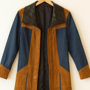 Puede incluir: Un abrigo largo y abierto con un llamativo diseño de bloques de color. El abrigo presenta mangas y paneles traseros de mezclilla azul, complementados con paneles marrones de imitación de ante. El cuello es de cuero sintético negro acolchado. Tachuelas plateadas adornan el cuello y los puños.