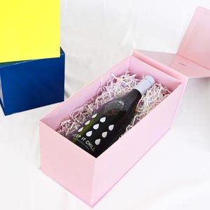 May include: A black wine bottle with white raindrop graphics and the text "KEEP IT CHILL" inside a pink gift box with shredded paper. Other boxes are blue and yellow.