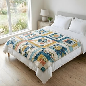 Può includere: Una trapunta colorata con un design patchwork, con forme geometriche e motivi floreali nei toni del blu, giallo, pesca e crema. La trapunta è posizionata su un letto con biancheria da letto bianca, creando un'atmosfera accogliente. Le dimensioni della trapunta non sono visibili.