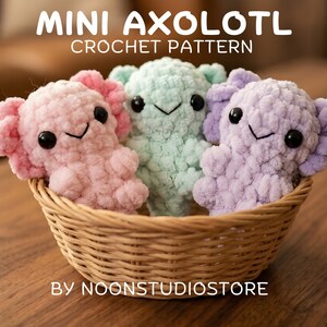 May include: Three crocheted axolotls in a woven basket. The axolotls are pink, mint green, and lavender, each with black eyes and a smiling mouth. The text "MINI AXOLOTL CROCHET PATTERN" is at the top, with "BY NOONSTUDIOSTORE" at the bottom.