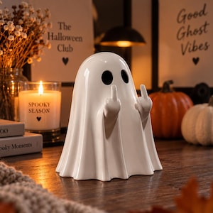 Peut inclure: Une figurine de fantôme en céramique blanche brillante avec deux grands yeux ovales noirs et deux bras levés montrant les majeurs. Le fantôme présente un aspect lisse rappelant un drapé avec des plis verticaux à la base, posé debout.