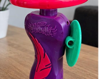 Peut inclure: Un lanceur de jouet Nerf Rebelle violet avec un composant supérieur circulaire rose vif, un accent en forme de plume rose sur le côté et une pièce latérale circulaire verte. Le mot Nerf Rebelle est gravé sur le corps en plastique violet.