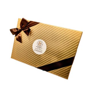 Op de afbeelding: Een gouden doos met een bruin lint en een wit rond label met de tekst "Artisan Bonbons 24 Stuks Classic Collection".
