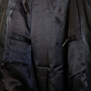 May include: Close-up of the interior of a black leather jacket. The lining is a dark, satiny fabric with a pocket on the left side. A zipper pocket is visible on the right side. The jacket appears to be well-worn.