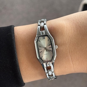 Pu&ograve; includere: Orologio al quarzo color argento con quadrante rettangolare e bracciale a maglie argentate. Il quadrante dell'orologio &egrave; di colore chiaro con lancette nere e numeri romani. La parola "QUARTZ" &egrave; stampata sul quadrante.