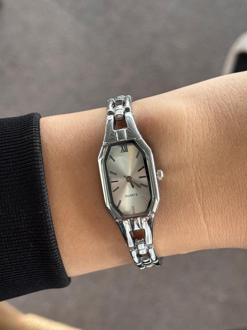 Pu&ograve; includere: Orologio al quarzo color argento con quadrante rettangolare e bracciale a maglie argentate. Il quadrante dell'orologio &egrave; di colore chiaro con lancette nere e numeri romani. La parola "QUARTZ" &egrave; stampata sul quadrante.