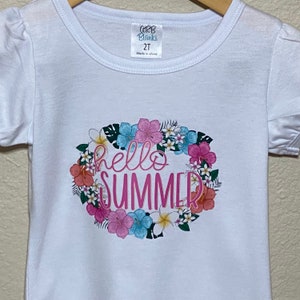 A close up view of the Hello Summer floral design on the front of the white tee shirt with the short puff sleeves.