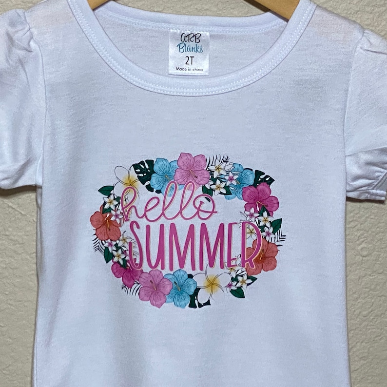 A close up view of the Hello Summer floral design on the front of the white tee shirt with the short puff sleeves.