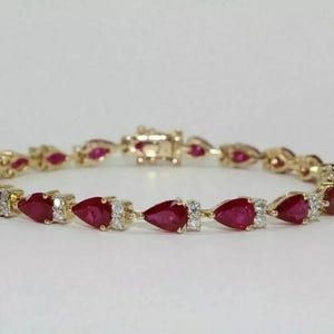 Puede incluir: Una pulsera dorada con piedras preciosas rojas en forma de pera y pequeñas piedras blancas. La pulsera se asegura con un cierre y se muestra sobre un fondo blanco. Esta elegante joya es adecuada para ocasiones especiales.