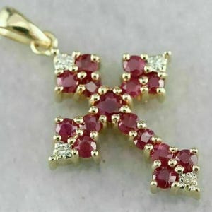 May include: A gold-colored pendant in the shape of an arrow, encrusted with small, round, deep red rubies. The pendant also features small clusters of white diamonds. The bail is also gold-colored.