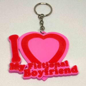 May include: A pink and red keyring with the text "I My Fictional Boyfriend" in red. The keyring features a heart shape and a silver metal ring and chain.