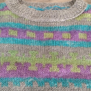 May include: Close-up of a gray knitted sweater with a round collar. The sweater features horizontal stripes in teal, purple, and green, with a textured pattern. The collar has a gray, textured design with teal accents.