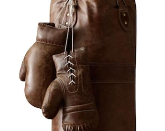 May include: A brown leather punching bag and boxing gloves. The gloves, laced with white, hang in front of the bag. The bag is cylindrical and suspended from a metal hook. The leather has a distressed appearance.