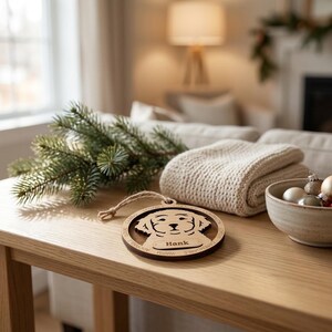 May include: A circular wooden ornament featuring a laser-cut dog silhouette and the name Hank engraved on a central plaque. The border includes engraved words such as Adorable, Loyal, Caring, Friendly, and Dependable, with a jute twine loop.
