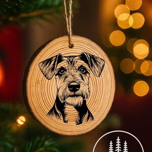 Puede incluir: Un adorno redondo de madera con una detallada ilustración en blanco y negro de la cara de un perro. El adorno está colgado de una cuerda de hilo. La esquina inferior derecha tiene un logotipo que dice "WestCoast Wood Working & Laser-Art".