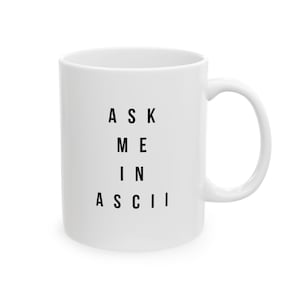 Könnte beinhalten: Ein weißer Keramikbecher mit glatter Oberfläche und einem geschwungenen Henkel auf der rechten Seite. Auf der Vorderseite ist der schwarze Text ASK ME IN ASCII in einer klaren serifenlosen Schrift in vier zentrierten Zeilen aufgedruckt.