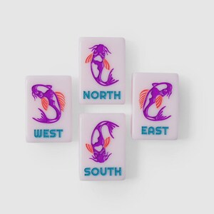 Puede incluir: Cuatro fichas de mahjong rectangulares de color morado claro dispuestas en forma de cruz. Cada ficha presenta una ilustraci&oacute;n de un pez koi morado con aletas naranjas y el texto de direcci&oacute;n NORTH, SOUTH, EAST o WEST en letras azul brillante.
