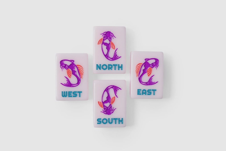 Puede incluir: Cuatro fichas de mahjong rectangulares de color morado claro dispuestas en forma de cruz. Cada ficha presenta una ilustraci&oacute;n de un pez koi morado con aletas naranjas y el texto de direcci&oacute;n NORTH, SOUTH, EAST o WEST en letras azul brillante.