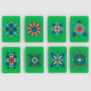 May include: Eight rectangular green tiles arranged in two rows of four. Each tile features a unique, symmetrical floral or geometric pattern rendered in raised, glossy paint in shades of blue, pink, red, and black, creating a decorative set.