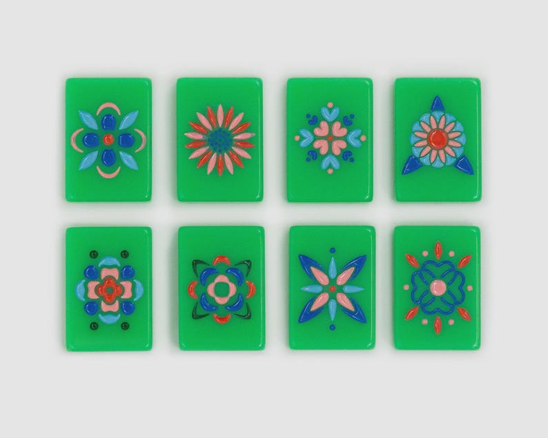 May include: Eight rectangular green tiles arranged in two rows of four. Each tile features a unique, symmetrical floral or geometric pattern rendered in raised, glossy paint in shades of blue, pink, red, and black, creating a decorative set.