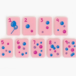 May include: A set of nine rectangular light pink tiles, each featuring a dark pink numeral from one to nine. The tiles are decorated with various blue and dark pink circular bubble designs, with the first tile showing a bubble wand.