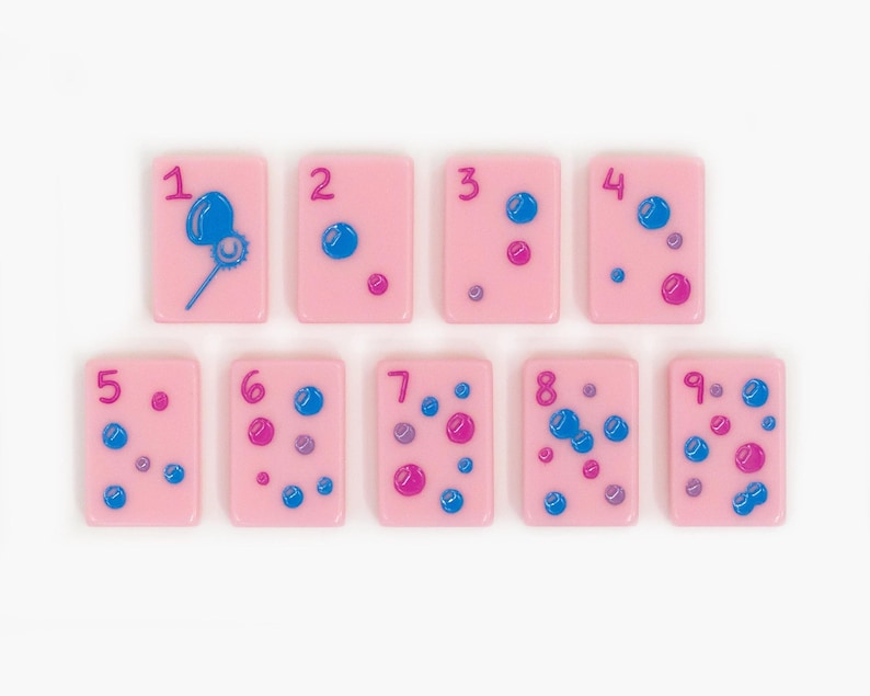 May include: A set of nine rectangular light pink tiles, each featuring a dark pink numeral from one to nine. The tiles are decorated with various blue and dark pink circular bubble designs, with the first tile showing a bubble wand.
