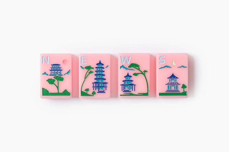 Puede incluir: Cuatro fichas de mahjong rectangulares de color rosa dispuestas horizontalmente. Cada ficha presenta un grabado azul y verde de una pagoda, &aacute;rboles y monta&ntilde;as. Las letras N, E, W y S est&aacute;n impresas en azul claro en cada ficha.