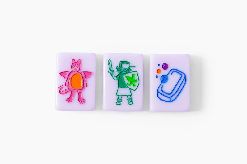Pu&ograve; includere: Tre piastrelle rettangolari color viola chiaro con disegni colorati in rilievo. La prima piastrella mostra un drago rosa con la pancia arancione. La seconda raffigura una figura con una spada e uno scudo verde. La terza mostra una saponetta blu.