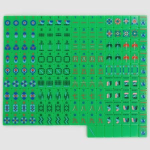 May include: A complete set of bright green mahjong tiles arranged in a grid. The tiles feature various colorful engraved designs including numeric characters, bamboo patterns, circular symbols, directional markers, and floral motifs in blue, red, and pink.