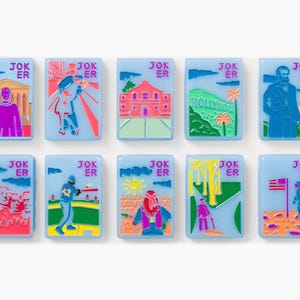 Puede incluir: Un conjunto de diez fichas rectangulares de color azul claro, cada una con la palabra JOKER en letras rosas. Las fichas presentan ilustraciones gr&aacute;ficas coloridas de monumentos e iconos culturales estadounidenses, incluyendo el Monte Rushmore, un jugador de b&eacute;isbol y un astronauta.