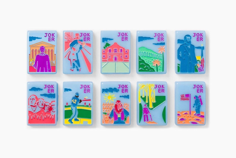 Puede incluir: Un conjunto de diez fichas rectangulares de color azul claro, cada una con la palabra JOKER en letras rosas. Las fichas presentan ilustraciones gr&aacute;ficas coloridas de monumentos e iconos culturales estadounidenses, incluyendo el Monte Rushmore, un jugador de b&eacute;isbol y un astronauta.