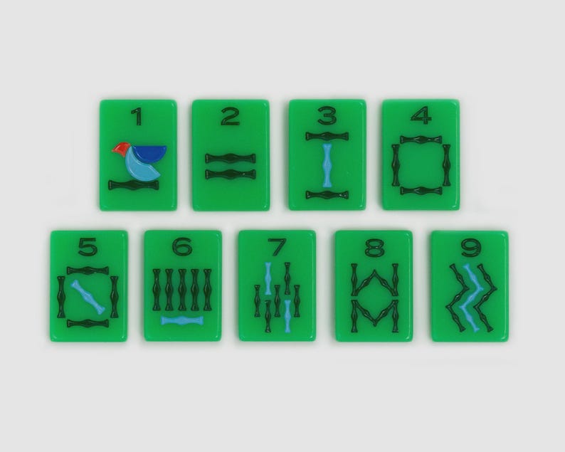 May include: A set of nine rectangular green Mahjong tiles arranged in two rows, numbered one through nine. Each tile features black and blue ink designs, with the number one tile displaying a small red, blue, and light blue bird graphic.