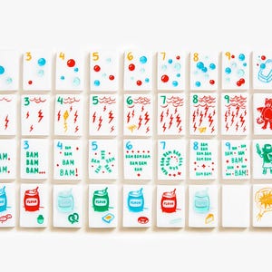May include: A set of rectangular white tiles arranged in four rows, featuring colorful hand-drawn illustrations and numbers. The designs include bubbles, lightning bolts, the text BAM, flour containers, food items, and cardinal directions.